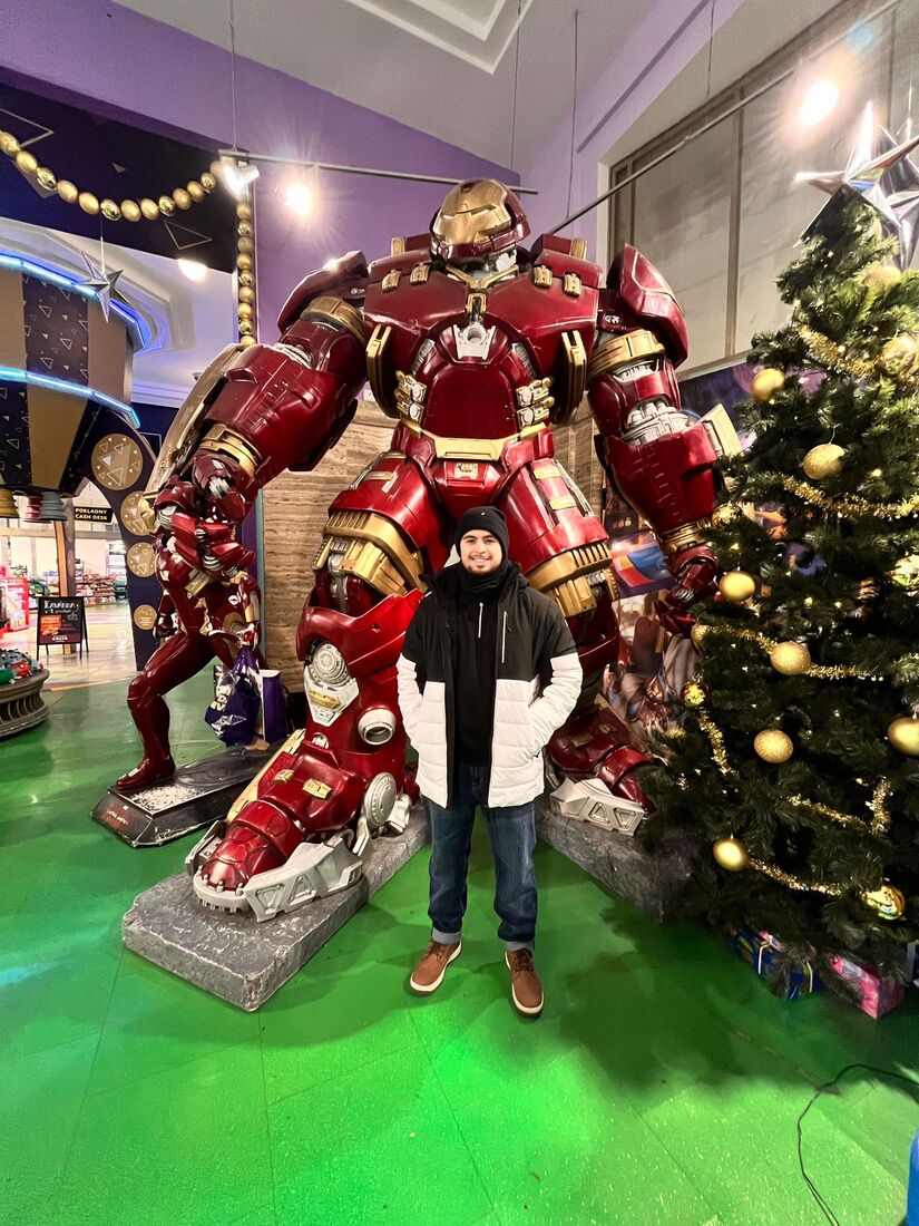 Sergio Gurillo, con gorro y abrigo, posando delante de una figura a tamaño real del Hulkbuster en un centro comercial decorado por Navidad